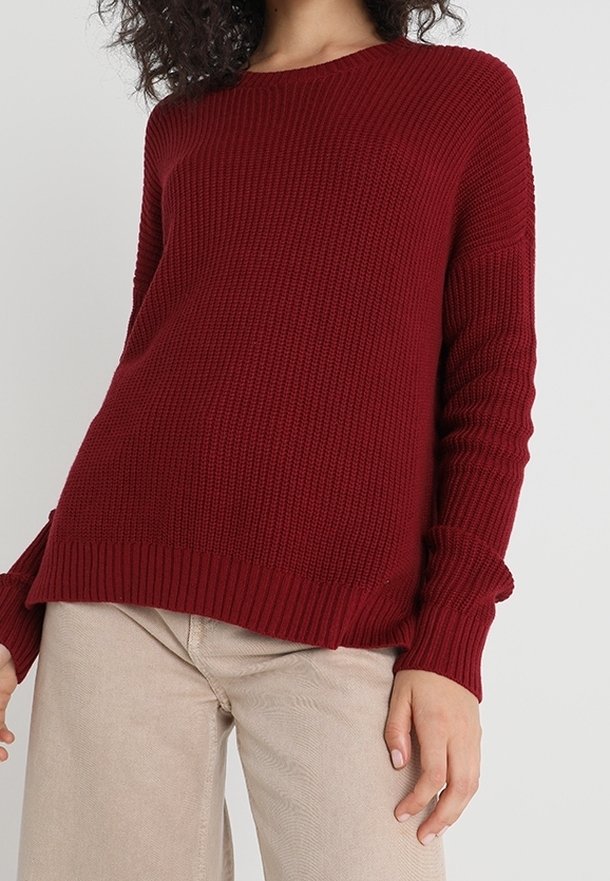 Pull en tricot bordeaux avec texture côtelée, encolure ronde et manches longues. Des fentes sur les côtés à l'ourlet ajoutent une coupe décontractée.