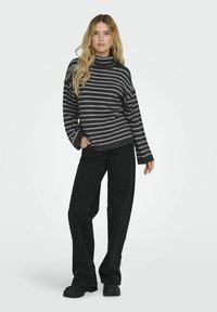 Gestreepte coltrui in donkergrijs en lichtgrijs, gecombineerd met zwarte wijde broek en zwarte schoenen. De trui heeft een ontspannen pasvorm.