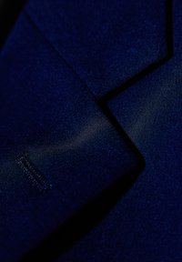 Tecido azul marino que muestra una solapa afilada con un sutil brillo, con finos detalles de costura a lo largo de los bordes y una textura suave.