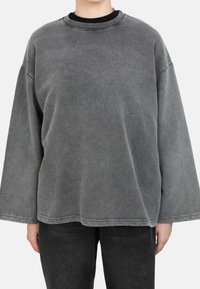 Oversized grijze sweatshirt met een ronde hals, verlaagde schouders en een zachte textuur. Gestyled met zwarte jeans voor contrast.