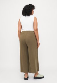 Olive green wide-leg pants with an elastic waistband, paired with a fitted white sleeveless top and light green footwear.