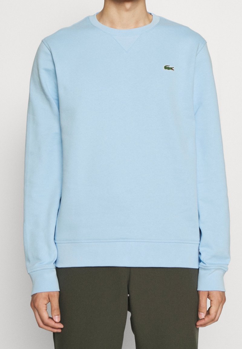 Ljusblå sweatshirt i mjuk bomull. Har rund halsringning, långa ärmar, ribbade muddar och nederkant, samt en liten grön logo på bröstet.