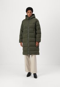 Long olive green puffer coat with a hood, zip closure, and side pockets, featuring a quilted design and a mid-length cut.