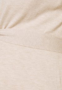 Beige gebreide top met een gedraaide ontwerp aan de voorkant. Zachte textuur, geribbelde zoom aan de onderkant en een gladde afwerking overal.