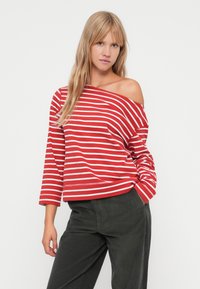 Red and white striped off-shoulder long-sleeve top with a relaxed fit, paired with dark green corduroy pants.