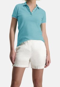 Polo bleu clair avec un col à trois boutons et des finitions roses, associé à un short en lin blanc, mettant en avant une coupe décontractée et une texture douce.