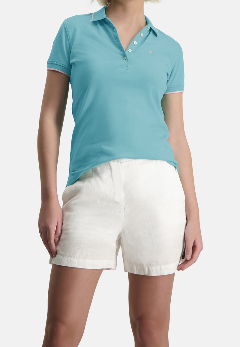 Polo bleu clair avec un col à trois boutons et des finitions roses, associé à un short en lin blanc, mettant en avant une coupe décontractée et une texture douce.