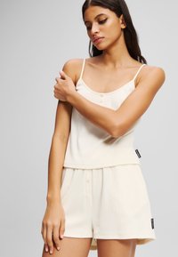 Kermanvärinen toppi ohuilla olkaimilla, jossa on napitettu etuosa, yhdistettynä vastaaviin shortseihin, molemmat pehmeää ribbikangasta.