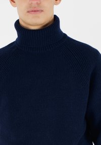Maglione a collo alto blu navy con texture a costine, caratterizzato da maniche raglan e un colletto alto. Il materiale sembra morbido e lavorato a maglia.