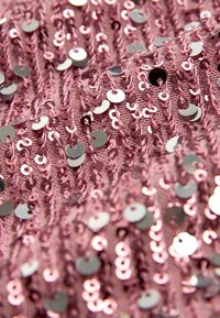 Krepovaná látka v jemně růžové barvě zdobená lesklými stříbrnými a duhovými flitry, které vytvářejí texturovaný, vrstvený vzhled.