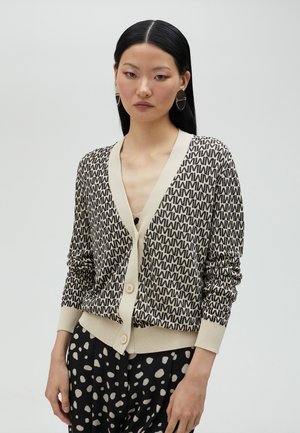 Beige cardigan with black abstract print, v-neckline, long sleeves, and two buttons at the front. Paired with patterned black pants.