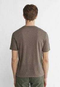 Braunes Kurzarm-T-Shirt aus weichem Material mit Rundhalsausschnitt. Der Rücken hat ein einfaches Design, zeigt klare Linien und keine Muster.