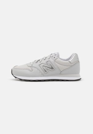 Zapatilla New Balance gris claro con suela blanca, parte superior de malla y piel, cierre de cordones y suela exterior negra texturizada.