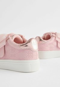 Rosa synthetische Sneakers mit einer strukturierten Oberfläche, die Schleifenmuster aufweisen, metallische Roségold-Akzente und eine weiße Gummisohle.