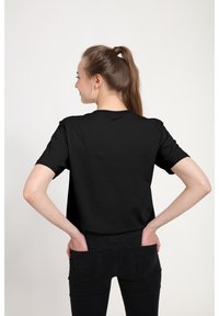 T-shirt noir à manches courtes en coton, avec un col rond et une coupe décontractée, associé à un jean noir, vu de l'arrière.
