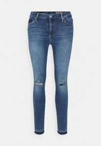 Jeans ajustados de denim azul claro, con desgastes en las rodillas, cinco bolsillos y un cierre de botón con cremallera.