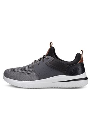 Zapatilla deportiva gris con parte superior de malla, paneles texturizados y suela blanca. Presenta acentos negros y una lengüeta marrón en el talón. Diseño ligero.