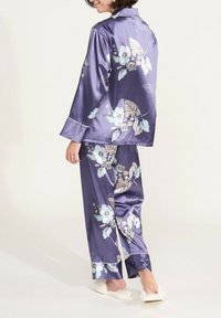 Ensemble de pyjama en satin violet avec un motif floral bleu et crème, arborant des passepoils contrastants sur les manches et les ourlets des pantalons.