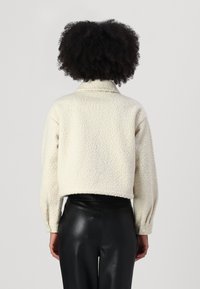 Cream, textured, fleece jacket with a collared neck and balloon sleeves; cropped design. Worn with fitted black faux leather pants.