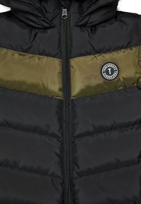 Giacca a vento nera con una banda orizzontale verde oliva, chiusura a zip nel davanti e una toppa rotonda con logo sul petto. Tessuto testurizzato con design trapuntato.