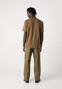 Brown short-sleeve t-shirt paired with olive green wide-leg pants. The fabric appears smooth with a relaxed fit and simple design.