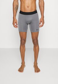 Sive športne kratke hlače iz raztegljive tkanine z črnim elastičnim pasom in logotipom Nike, zasnovane za udobje in svobodo gibanja.