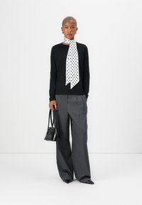 Black long-sleeve top, white polka dot scarf, gray pleated wide-leg trousers, and a small black handbag with pointed-toe shoes.