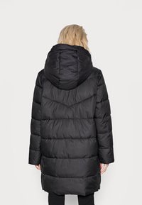 Sort pufferjakke med en stor hætte, kviltet design og lange ærmer. Har en lidt længere forkant og sidelukninger. Tekstileret stof.