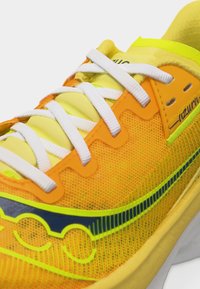 Φωτεινό κίτρινο και πορτοκαλί παπούτσι τρεξίματος με λευκά κορδόνια, επάνω μέρος από αεριζόμενο δίχτυ, και μπλε με νέον πράσινο λογότυπο στο πλάι.