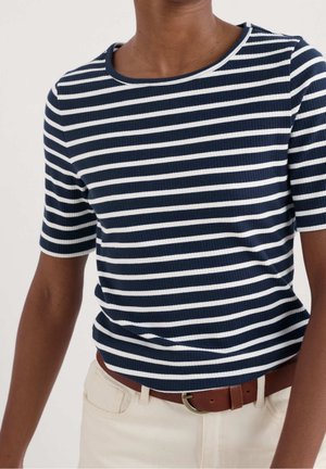 Person wearing a navy and white horizontal striped short-sleeve shirt tucked into light beige pants with a brown belt.