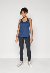Canottiera sportiva blu navy con scollatura arrotondata, abbinata a leggins neri e scarpe da corsa grigie con accenti bianchi.