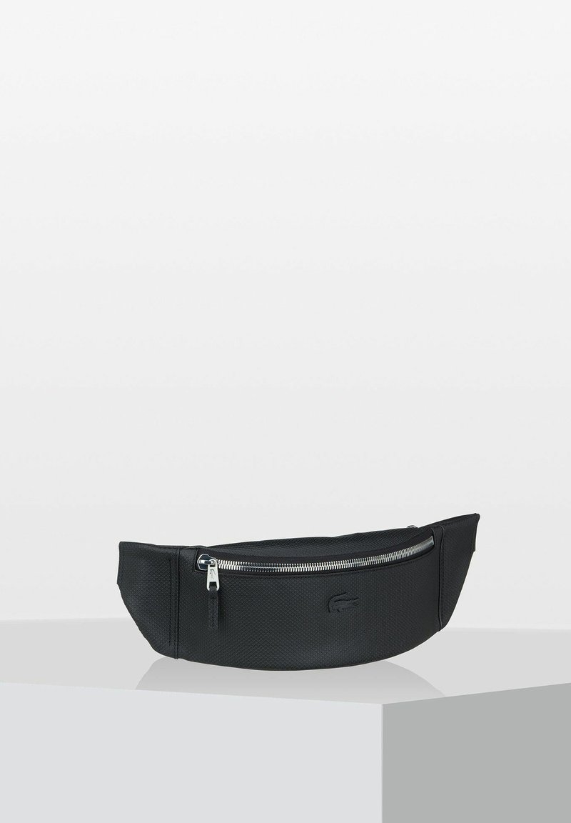 Sac à taille en tissu noir avec une surface texturée, une forme courbée et une poche zippée à l'avant. Il est doté de quincaillerie argentée et d'un logo subtil.