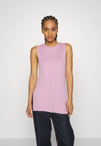 Top rosa canelado sem mangas com decote redondo, apresentando um corte reto e fendas laterais, combinado com calças largas de denim escuro.