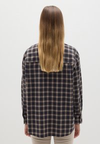 Camisa de franela a cuadros en tonos marino y beige, con un corte relajado, cierre de botones en la parte delantera y mangas largas. Textura suave con una abertura en la parte posterior.