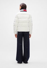 Balta pūkinė striukė su horizontaliu siuvinėjimu, susiglaudusiomis rankovėmis ir tamsiai mėlynu, raudonu bei baltu dryžuotu apykakle. Dėvima su tamsiomis plačiomis džinsinėmis kelnėmis.