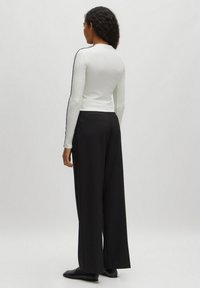 Witte longsleeve top met zwarte zijkanten, gecombineerd met losse zwarte broek. De top heeft een rechte pasvorm en een geribbelde textuur.
