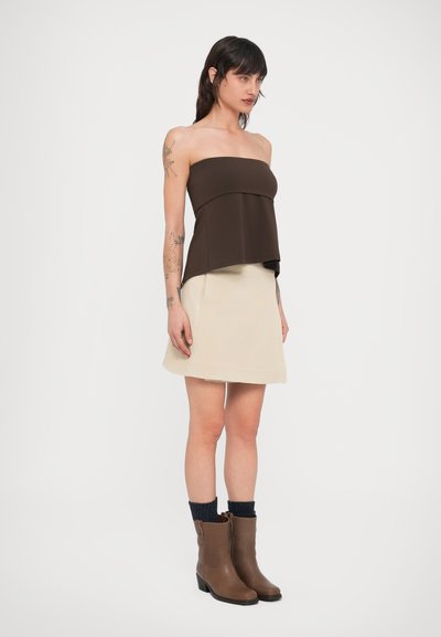 Καφέ τοπάκι χωρίς τιράντες με στρωματοποιημένο σχέδιο, σε συνδυασμό με ανοιχτό μπεζ μίνι φούστα και καφέ μποτάκια μέχρι τον αστράγαλο. Ορατές πλεκτές μπλε κάλτσες.