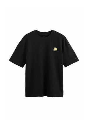 Melnas īsām piedurknēm T-krekls ar mazu dzeltenu kroni un uzrakstu "BASQUIAT" kreisajā krūtīs.