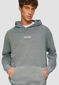 Szara bluza z kapturem wykonana z mieszanki bawełny, z przednią kieszenią typu kangurek i białym logo tekstowym. Luźny, casualowy styl.