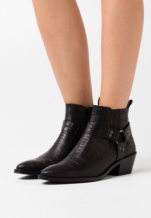 Stivaletti alla caviglia in pelle nera con motivo coccodrillo, punta appuntita, cerniera laterale e dettagli con fibbie in metallo sulla caviglia. Tacco basso a blocco.