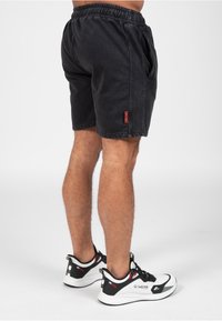 Zwarte denimshorts met een elastische tailleband, zijzakken en gestikte details. Gekozen in combinatie met witte sportschoenen met zwarte accenten.