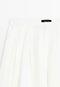 Pantalons en lin blanc à devant plat, avec des poches latérales et des plis, étiquetés d'une étiquette noire portant la mention "Massimo Dutti".