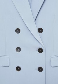 Blazer bleu clair à double boutonnage avec six boutons foncés et deux poches avant à rabat.