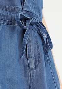 Garbato in denim con cintura annodata, di un blu profondo. Il tessuto presenta una finitura testurizzata con cuciture visibili e dettagli delle tasche.