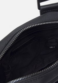 Interno di una borsa in tessuto nero con apertura con zip, fodera liscia e un piccolo anello metallico. Nessun scomparto visibile.