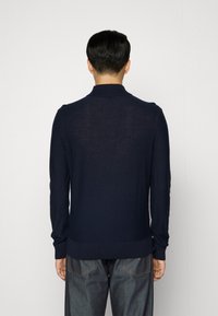 Marinblå stickad tröja med ribbad krage och ärmslut, med en strukturerad yta och slim fit-design. Bakåtsidan visar släta sömmar.