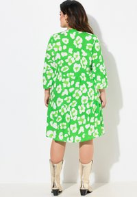 Grünes Kleid mit weißem abstraktem Muster, Dreiviertelärmel, gestufter Rock, weicher Stoff, kombiniert mit metallischen Stiefeletten.