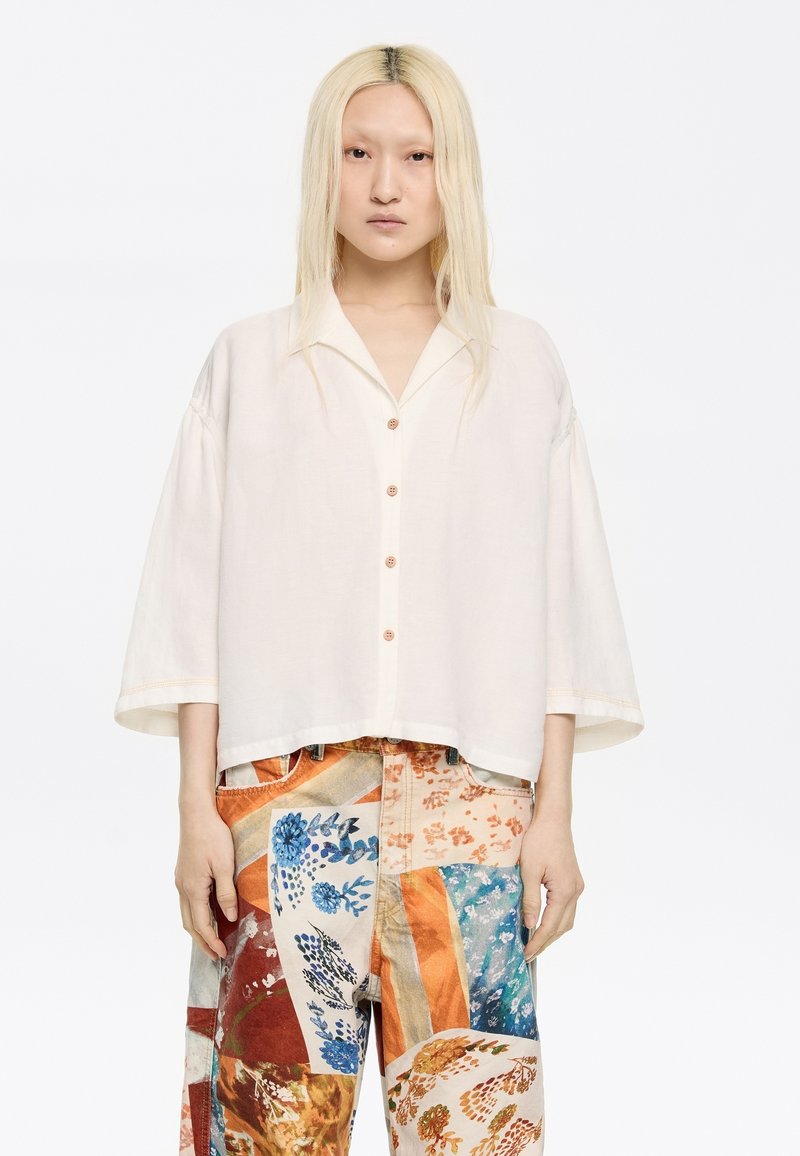 White, loose-fitting shirt with a collar and button front. Paired with multicolored patterned wide-leg pants featuring floral designs.