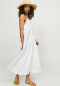 Vestido maxi blanco sin mangas con un corte holgado, tejido texturizado y un detalle en el dobladillo. Combinado con chanclas amarillas y un sombrero de paja.