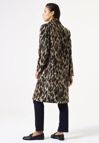 Luipaardprint jas met een zachte textuur, lange mouwen en een getailleerde pasvorm. Draagt met donkere jeans en zwarte loafers, wat een klassieke stijl toont.